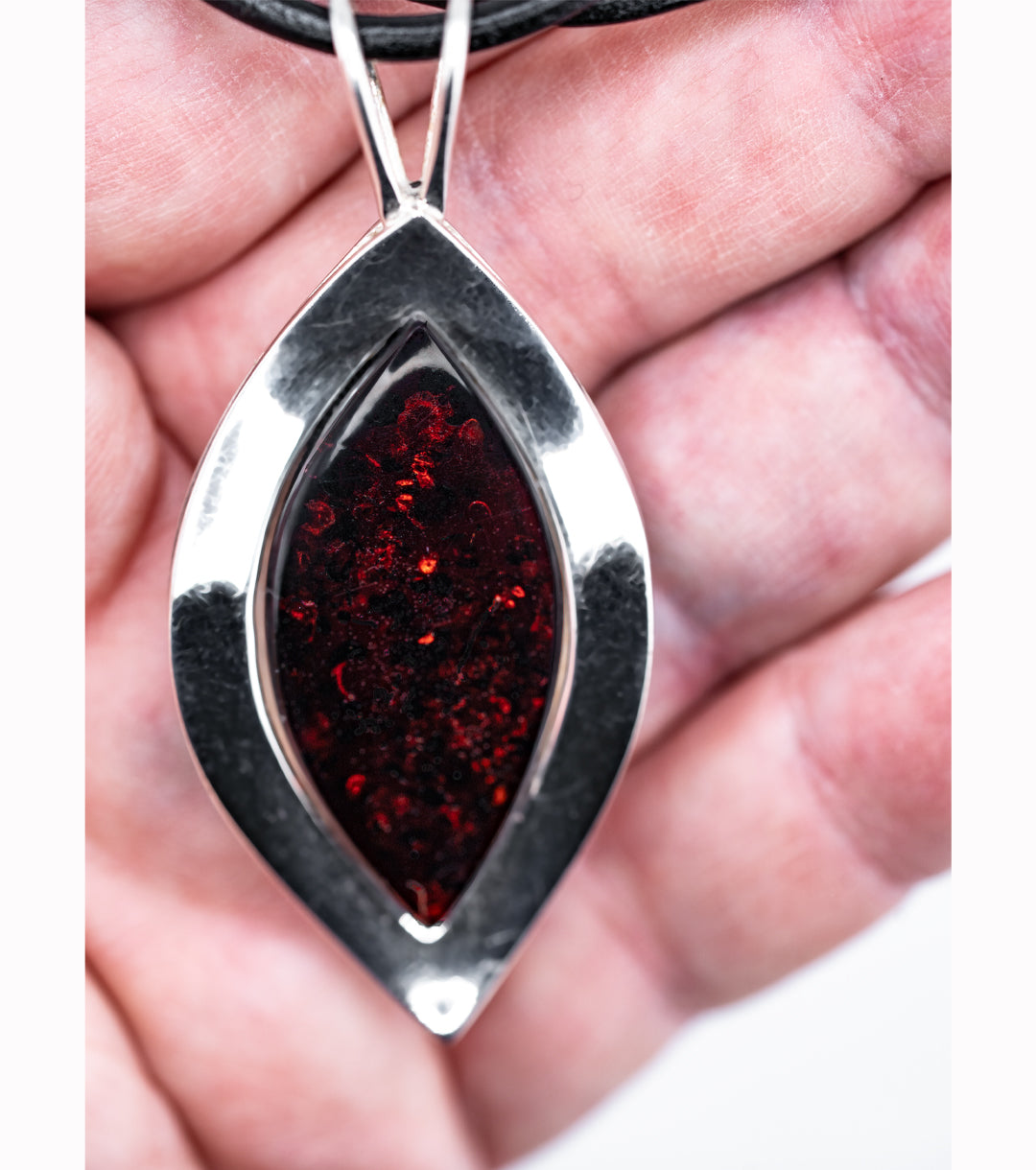 A close-up of a silver teardrop pendant with a dark red amber center, held in a person's hand.