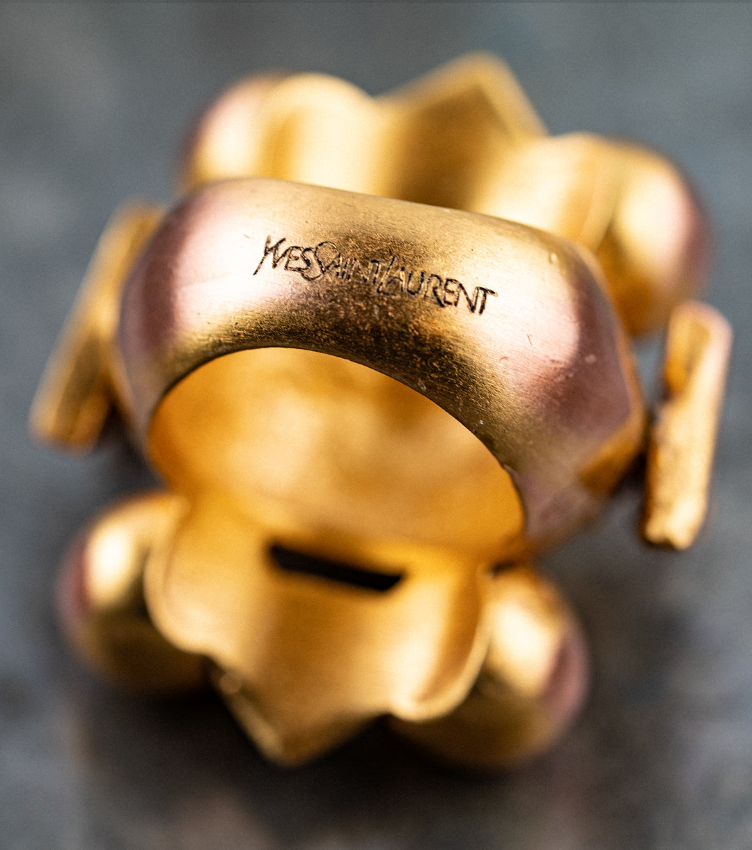 Gold ring with 'Yves Saint Laurent' engraving on a dark background